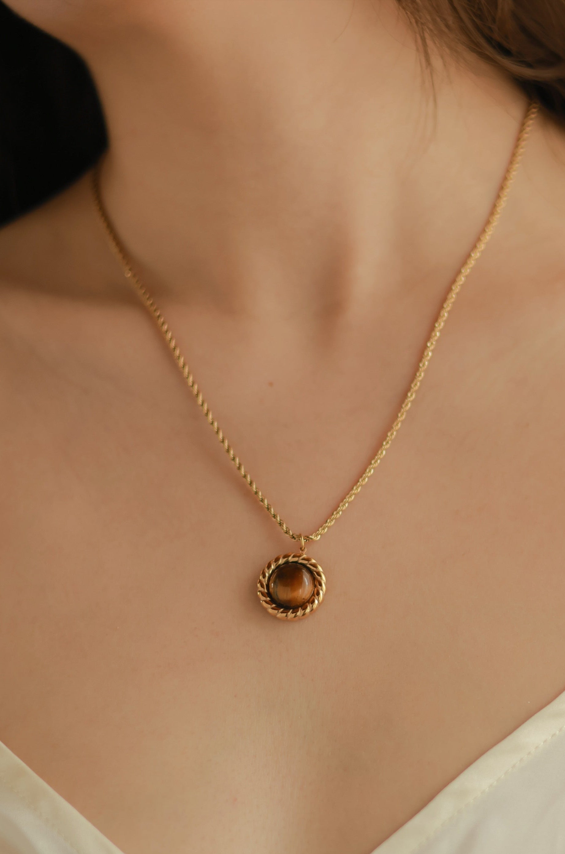 Close-up of a gold necklace with a pendant on a person wearing a light-colored top.